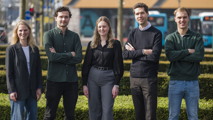Vijf trainees, 2 vrouwen en 3 mannen, staan zelfverzekerd buiten tegen en stedelijk decor met bomen en Arriva-bussen. Vijf trainees, 2 vrouwen en 3 mannen, staan zelfverzekerd buiten tegen en stedelijk decor met bomen en Arriva-bussen.