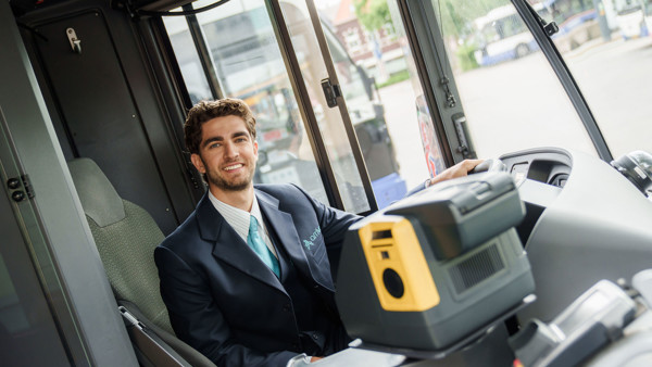 Een lachende buschauffeur in Arriva-uniform zit achter het stuur van een bus en kijkt naar de camera. Een lachende buschauffeur in Arriva-uniform zit achter het stuur van een bus en kijkt naar de camera.