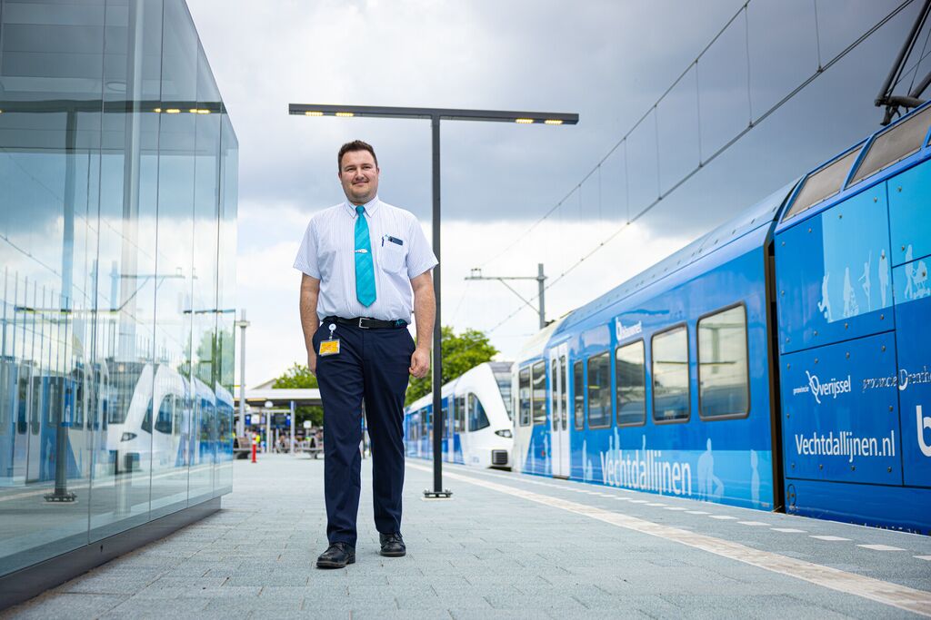 Mannelijke machinist loopt over een perron. Links een overdekte wachtruimte, rechts een Arriva-trein op het spoor.