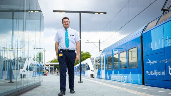 Mannelijke machinist loopt over een perron. Links een overdekte wachtruimte, rechts een Arriva-trein op het spoor. Mannelijke machinist loopt over een perron. Links een overdekte wachtruimte, rechts een Arriva-trein op het spoor.