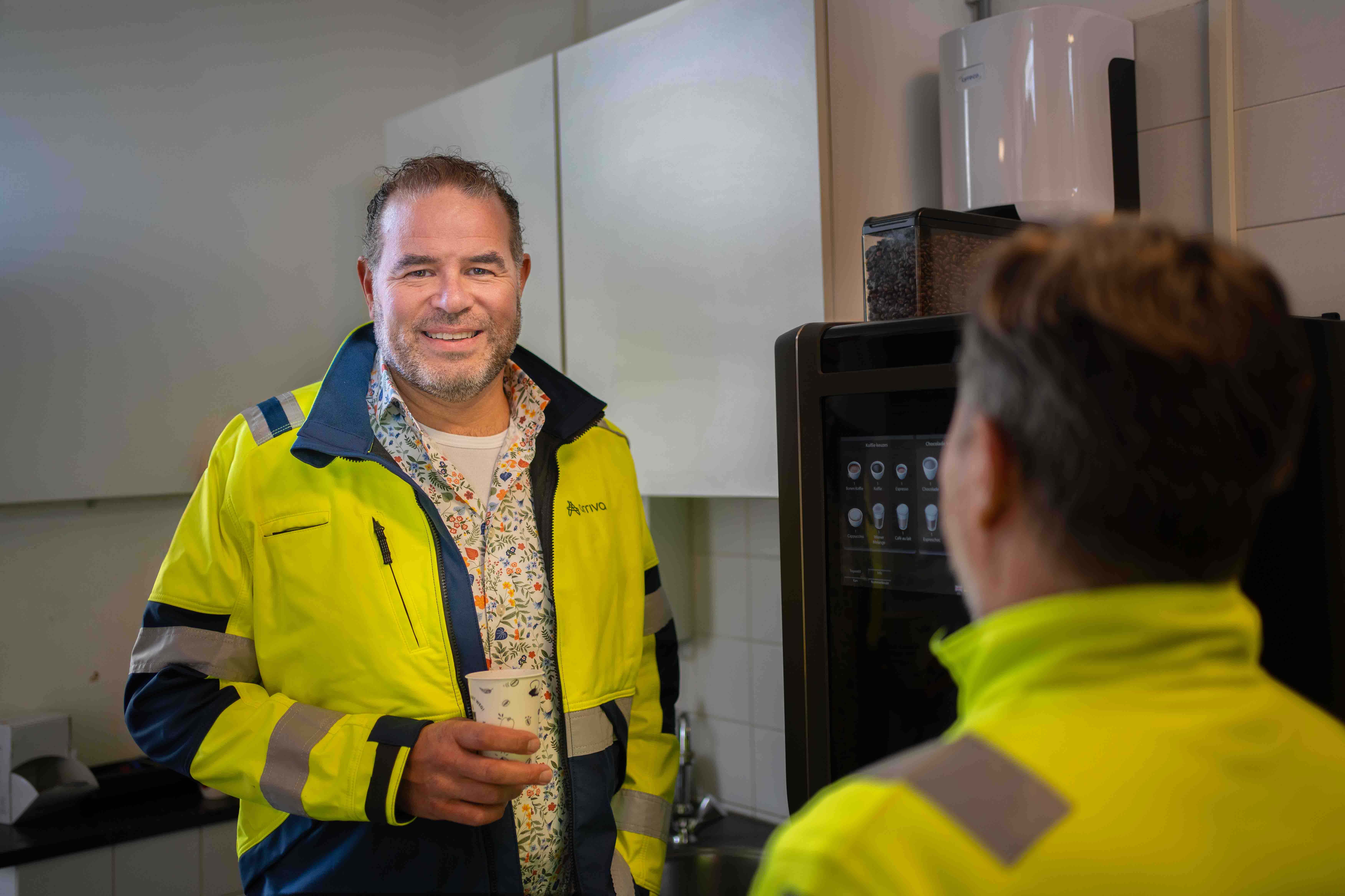 Teammanager Lars Sleijpen staat bij de koffieautomaat en lacht naar de camera