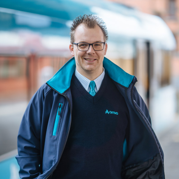 Machinist Frank staat lachend in Arriva-uniform op het perron, vaag in de achtergrond zie je een blauw-witte Arriva trein. Machinist Frank staat lachend in Arriva-uniform op het perron, vaag in de achtergrond zie je een blauw-witte Arriva trein.
