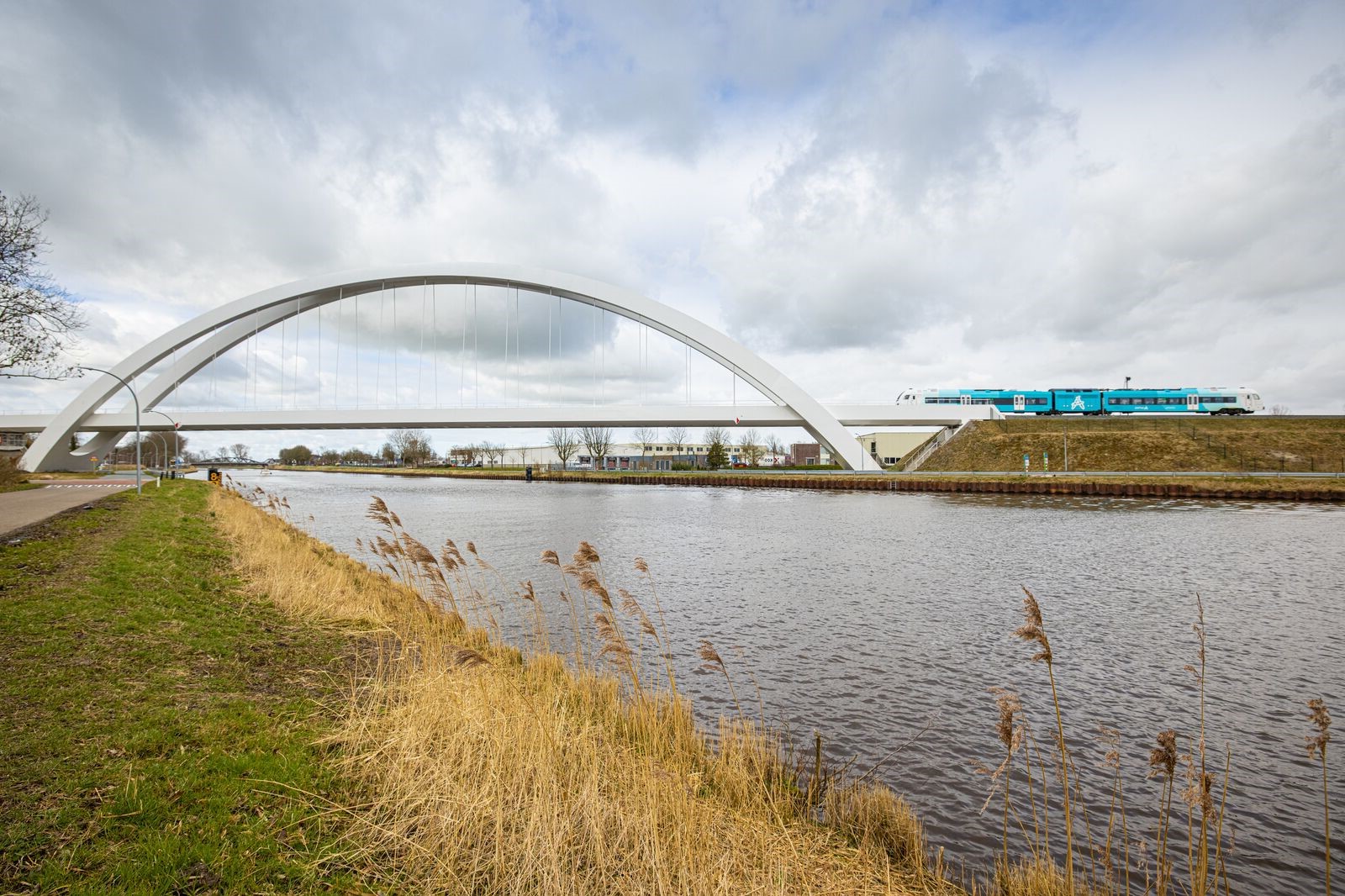 Een trein van Arriva rijdt richting een witte brug met hoge witte bogen.