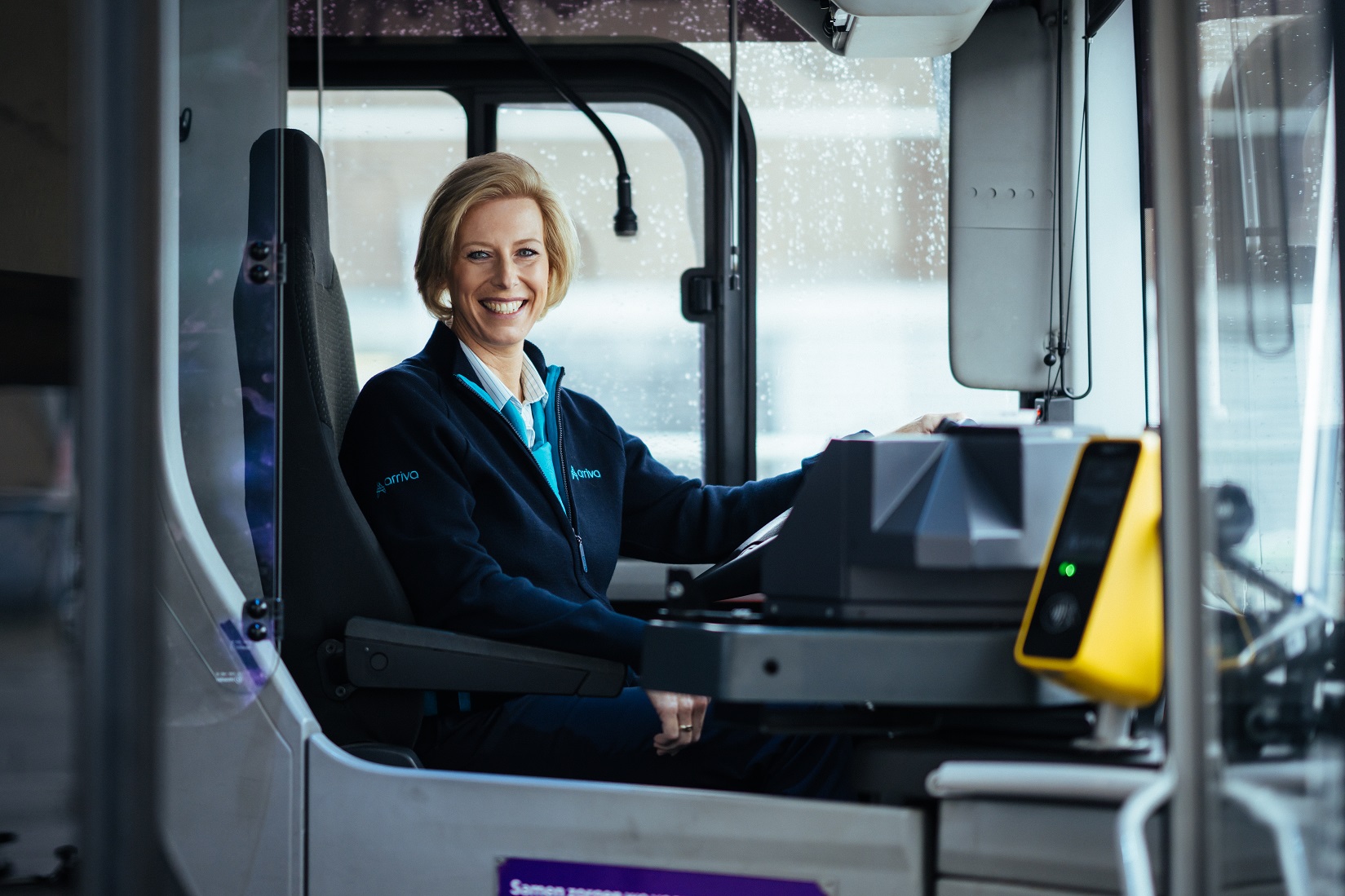 Buschauffeur Carola zit lachend achter het stuur van haar Arriva-bus.