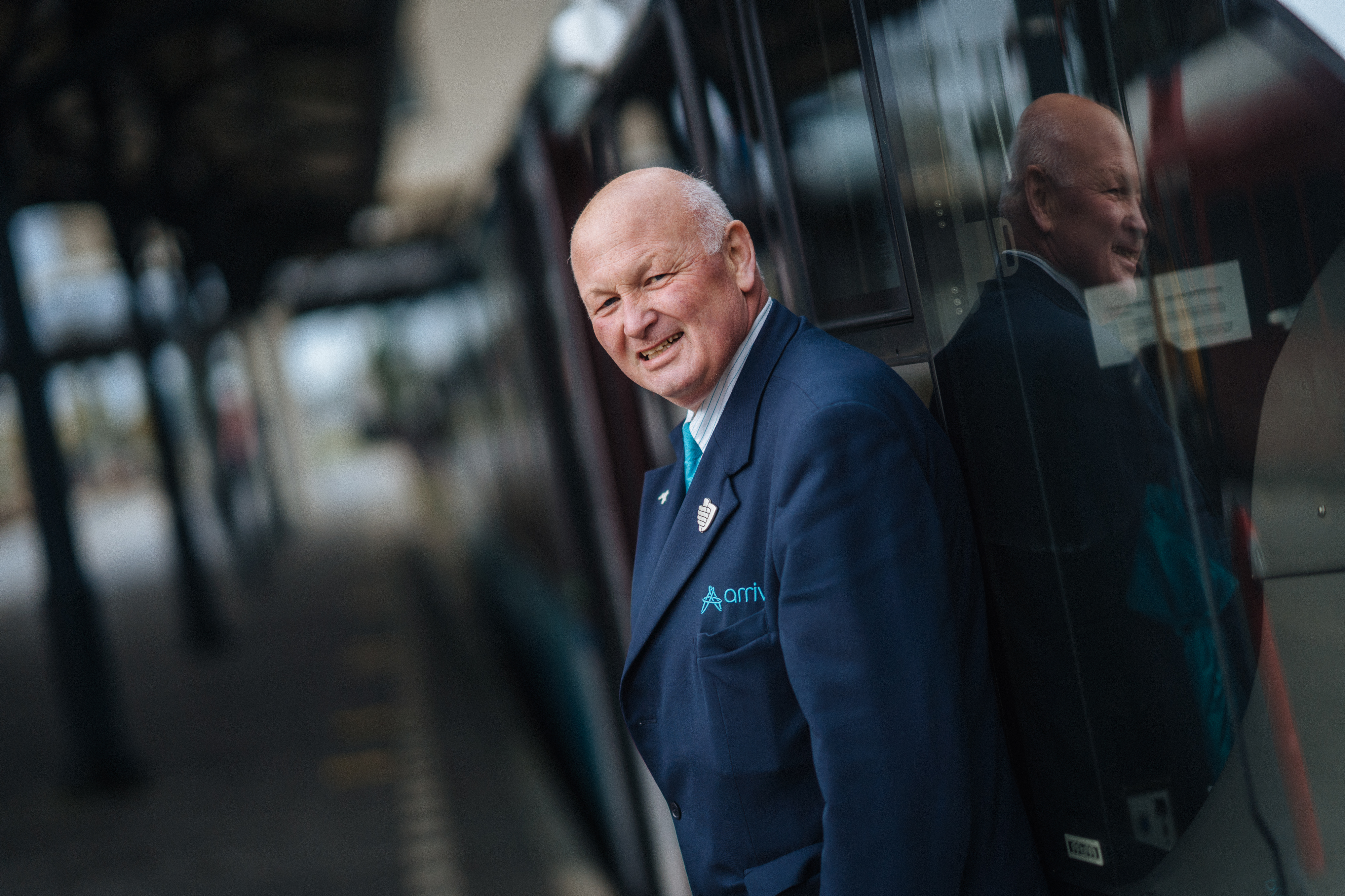 Steward Gerrie Drent staat lachend tegen een Arriva-trein geleund. 