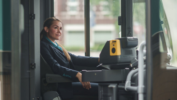 Een buschauffeur van Arriva zit in uniform achter het stuur van een stilstaande bus en kijkt dromerig in de verte. Een buschauffeur van Arriva zit in uniform achter het stuur van een stilstaande bus en kijkt dromerig in de verte.