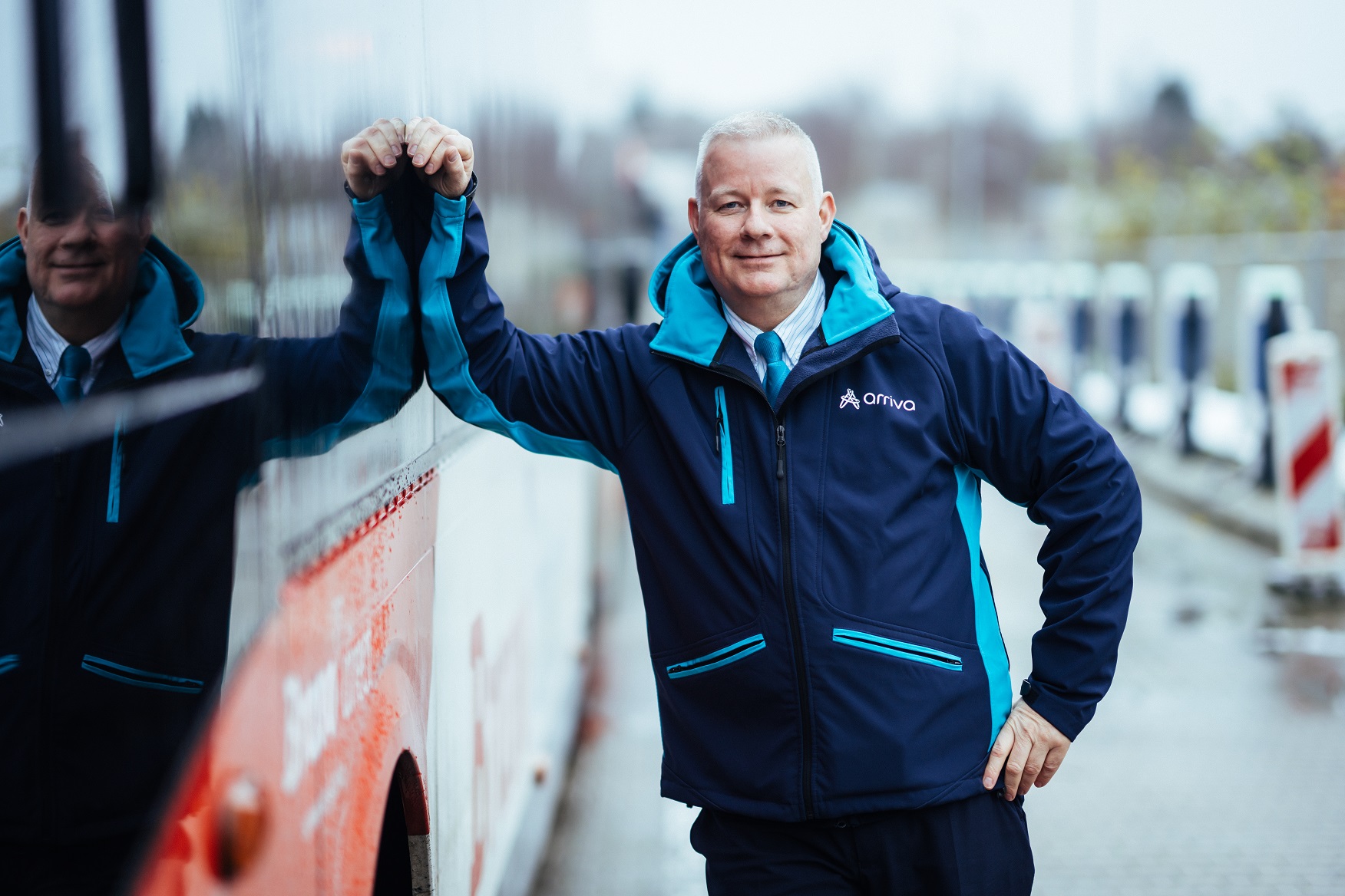 Buschauffeur Ron leunt relaxed en lachend tegen zijn Arriva-bus.