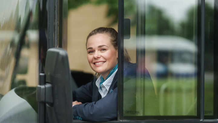 Buschauffeur in haar Arriva-uniform kijkt uit het zijraam van haar bus lachend naar buiten. Buschauffeur in haar Arriva-uniform kijkt uit het zijraam van haar bus lachend naar buiten.