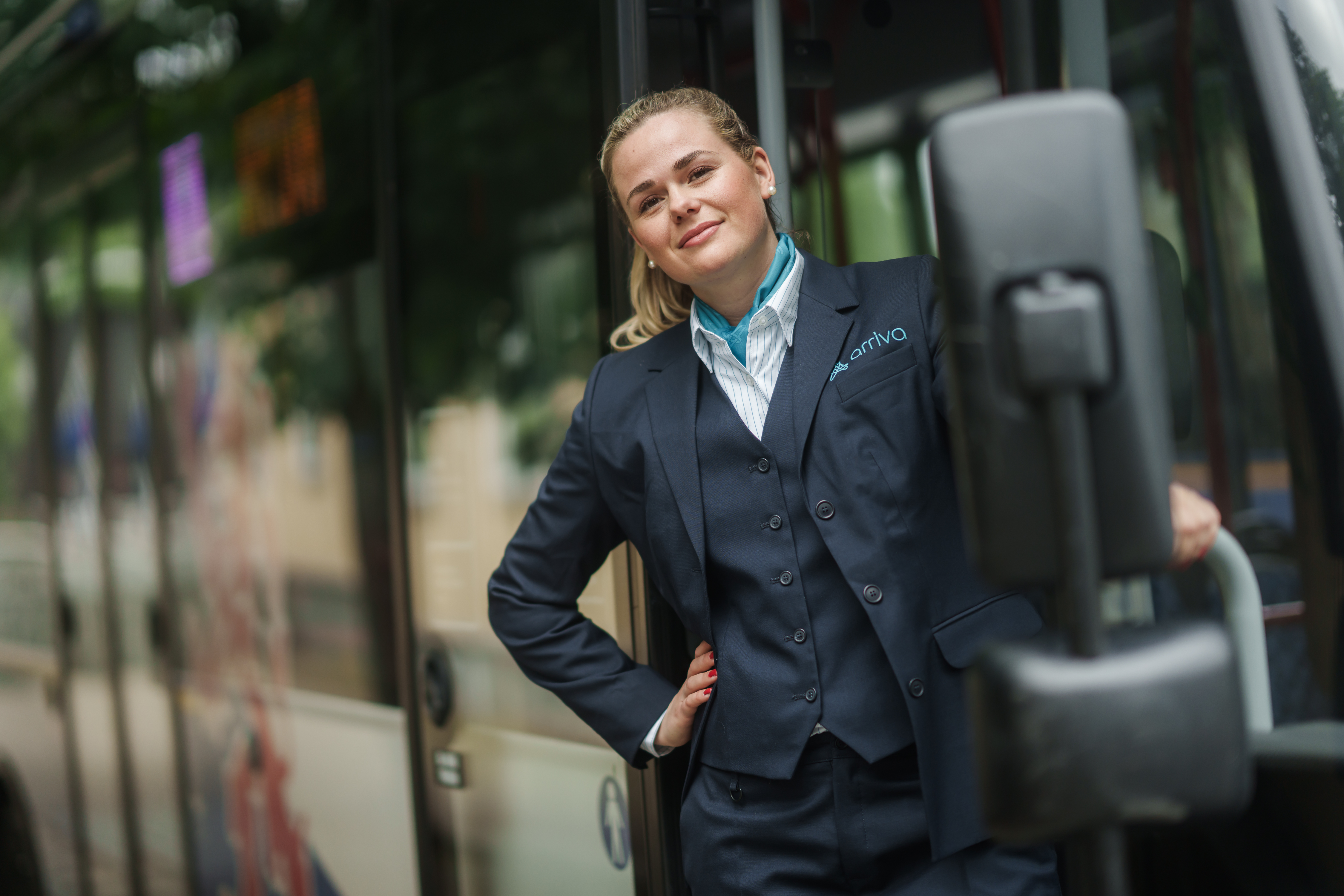 Buschauffeur hangt uit haar bus van Arriva en kijkt lachend in de camera.