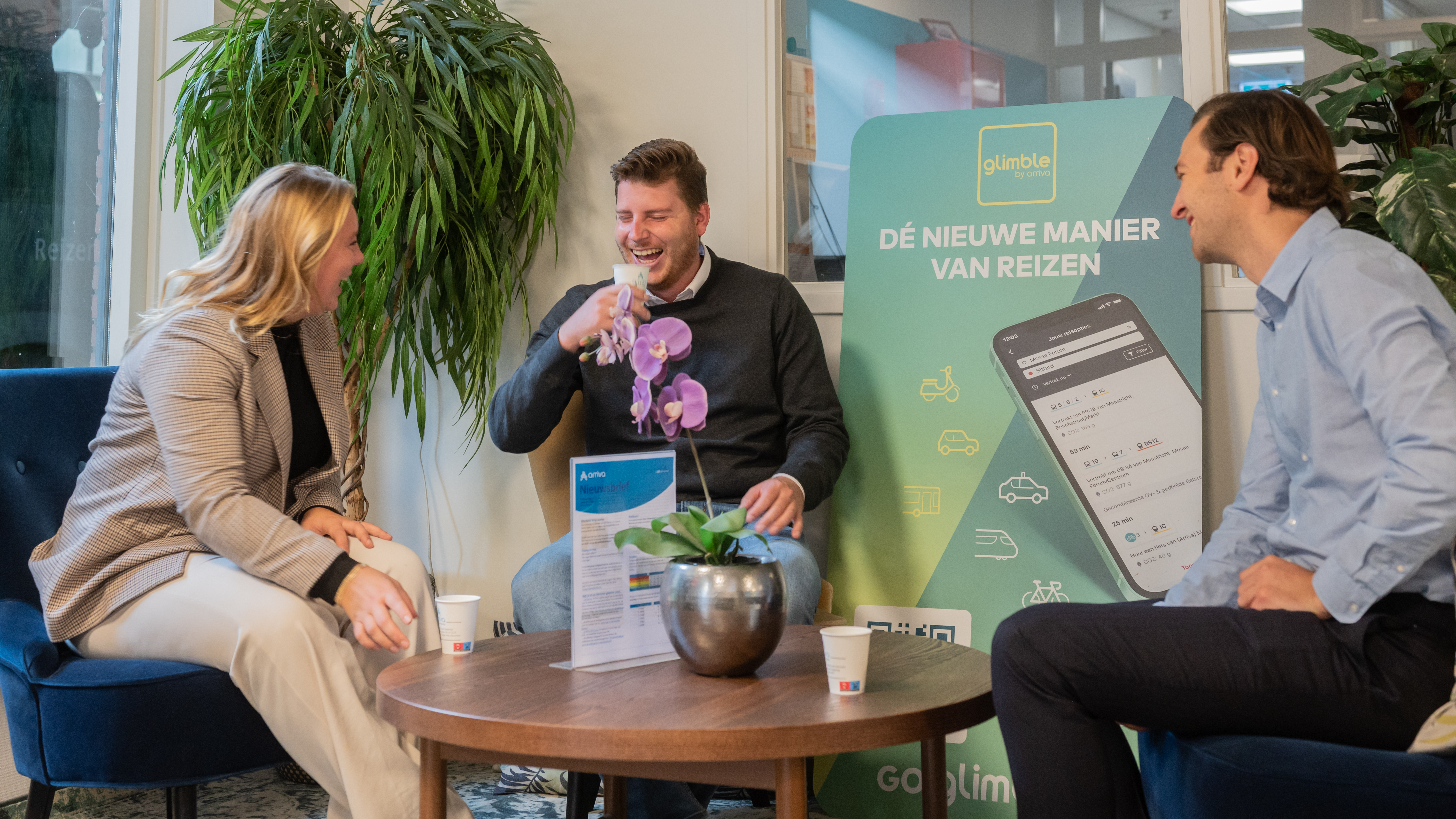 Drie jonge collega's van Arriva drinken samen koffie op kantoor en lachen.