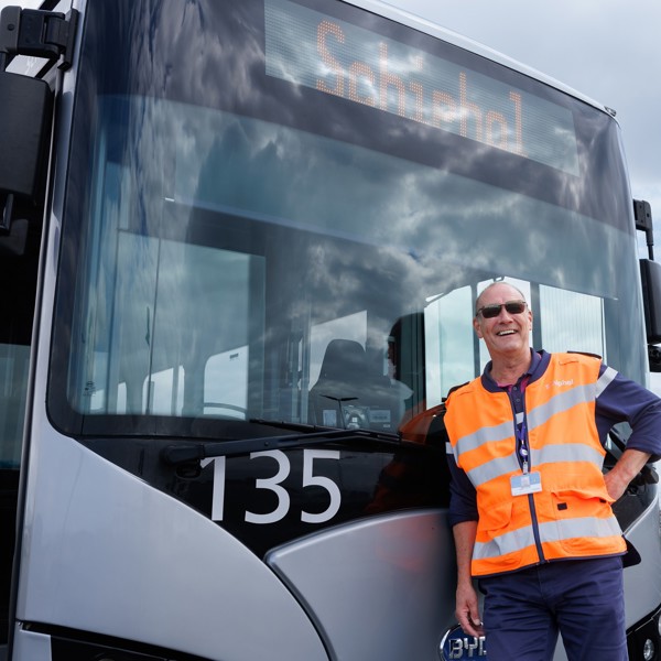 Buschauffeur in oranje hesje staat lachend voor Arriva Touringbus met Schiphol erop. Buschauffeur in oranje hesje staat lachend voor Arriva Touringbus met Schiphol erop.