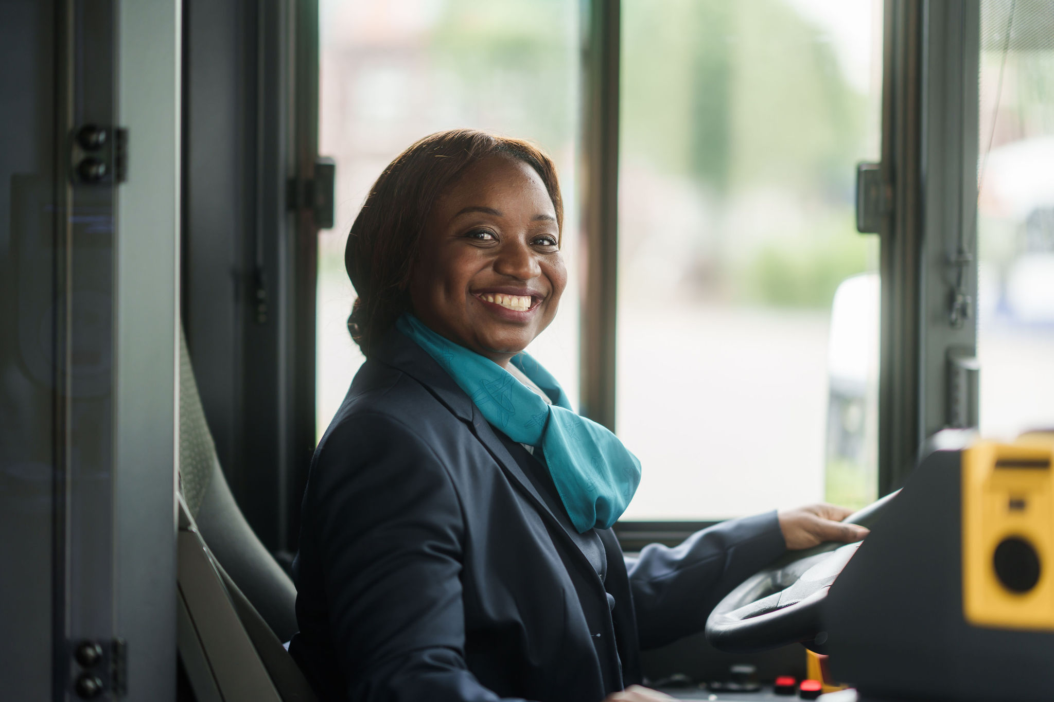 Buschauffeur in Arriva-uniform kijkt opzij en ze lacht naar de camera.