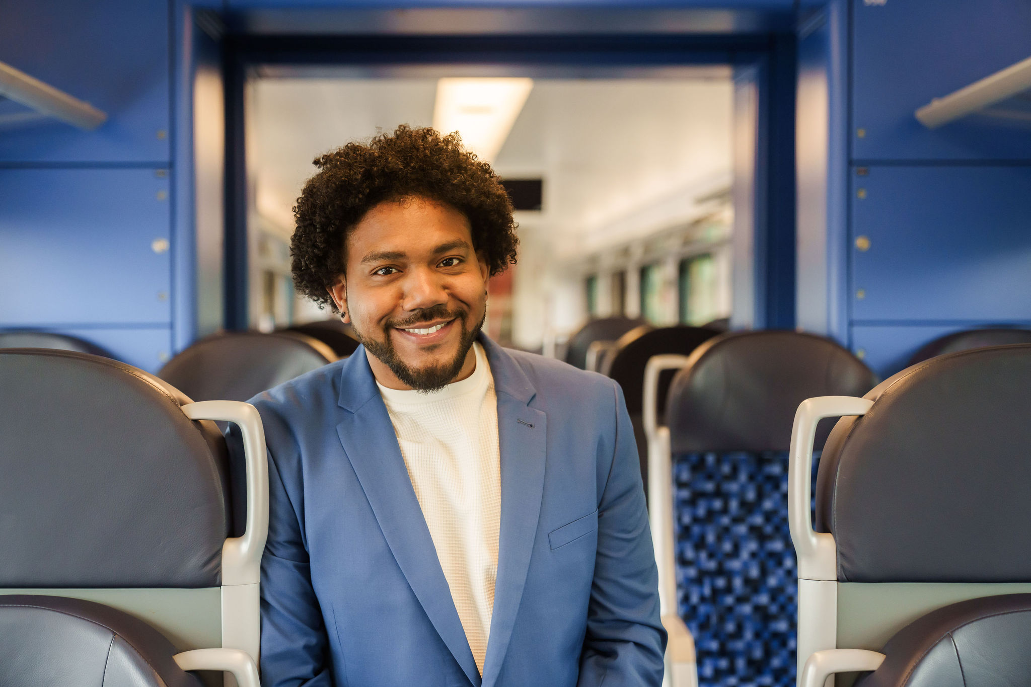 Een teammanager van Arriva staat tussen stoelen in de trein en lacht naar de camera.