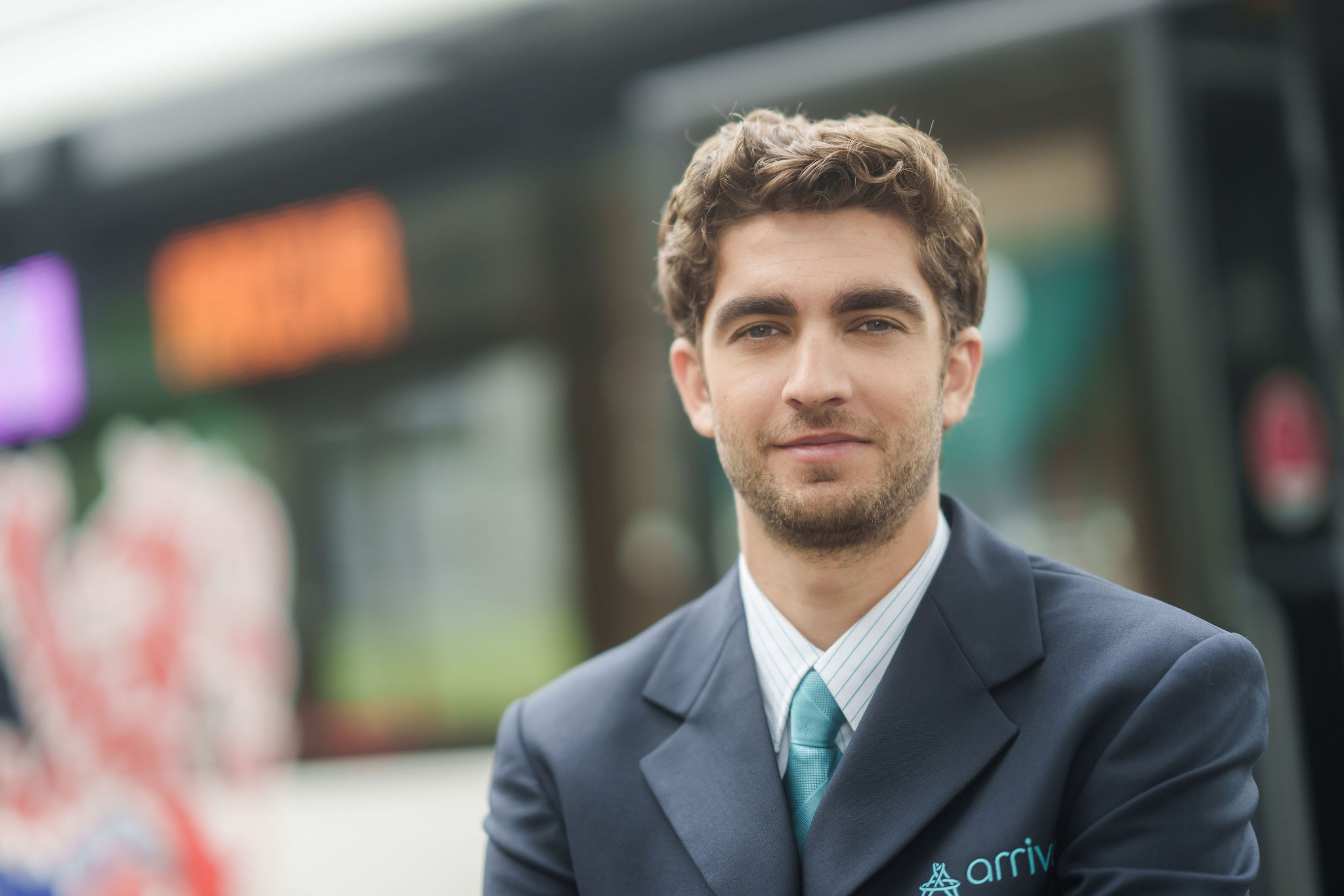 Buschauffeur van Arriva staat voor zijn bus en kijkt de camera in.