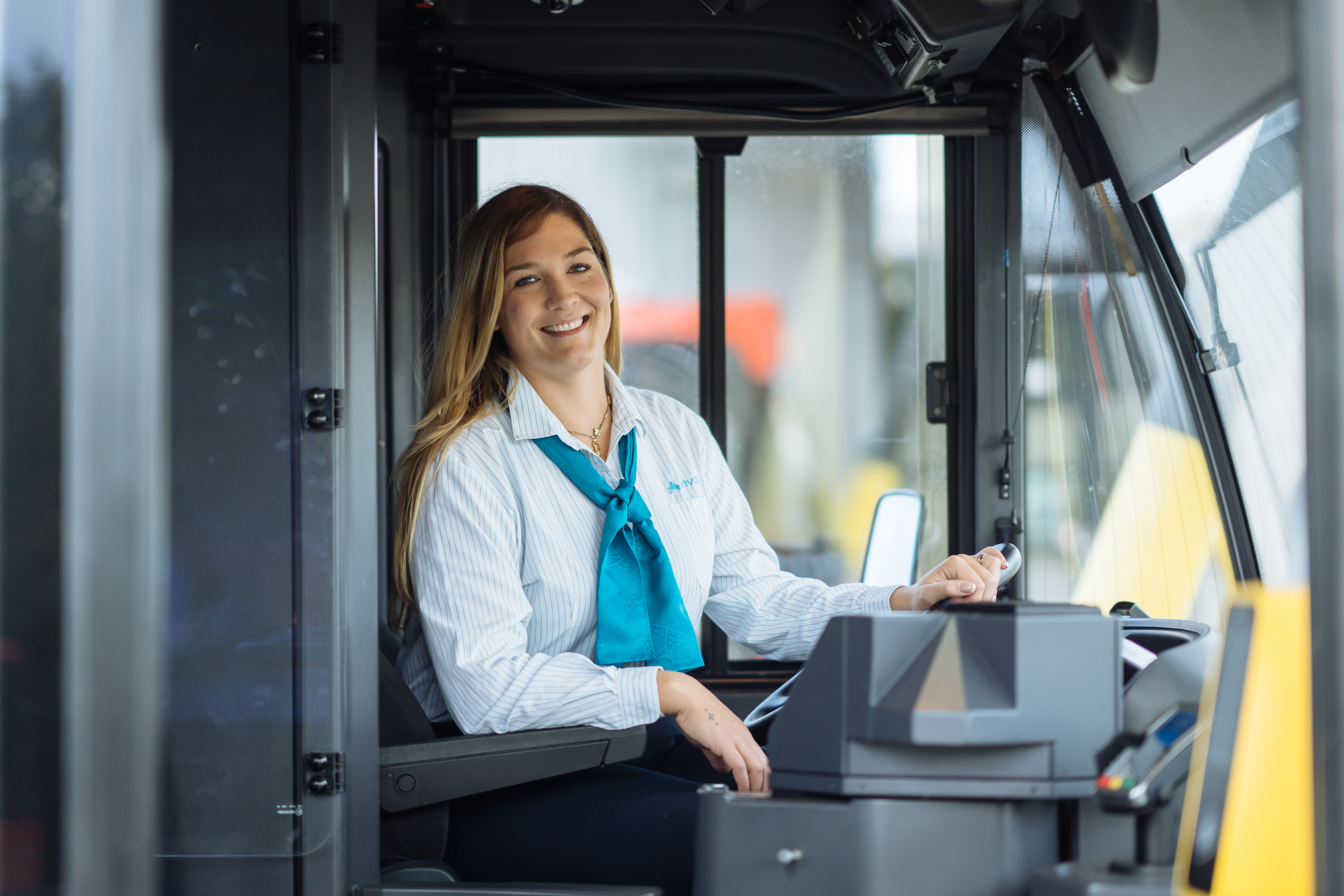 Jonge buschauffeur zit lachend achter het stuur van haar bus.