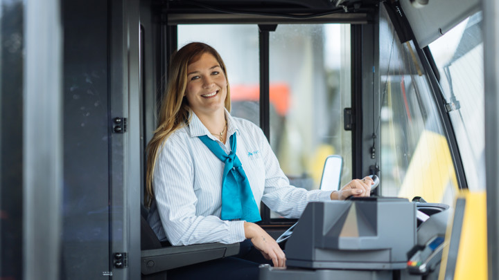 Jonge buschauffeur zit lachend achter het stuur van haar bus. Jonge buschauffeur zit lachend achter het stuur van haar bus.