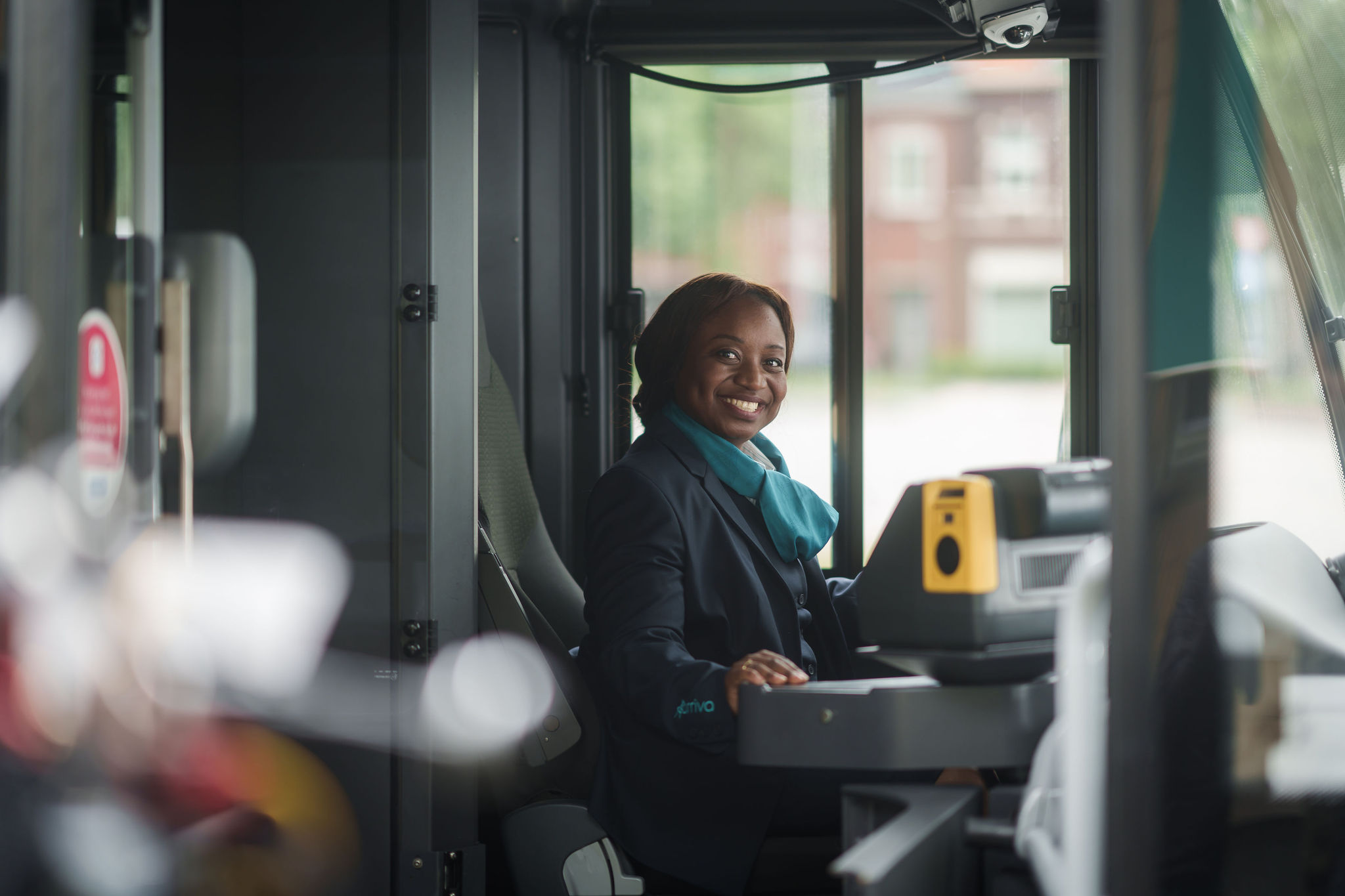 Een glimlachende buschauffeur in Arriva-uniform zit achter het stuur van een bus en kijkt naar de camera.