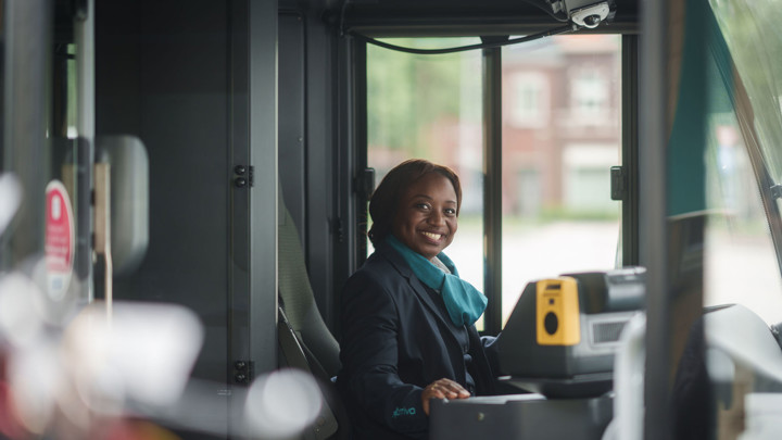 Een glimlachende buschauffeur in Arriva-uniform zit achter het stuur van een bus en kijkt naar de camera. Een glimlachende buschauffeur in Arriva-uniform zit achter het stuur van een bus en kijkt naar de camera.