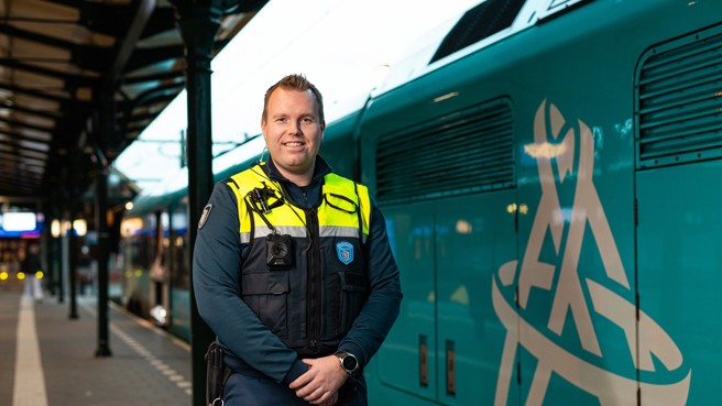 Een Steward/Boa OV staat in uniform en lachend op het perron, naast hem staat een blauwe Arriva-trein. Een Steward/Boa OV staat in uniform en lachend op het perron, naast hem staat een blauwe Arriva-trein.