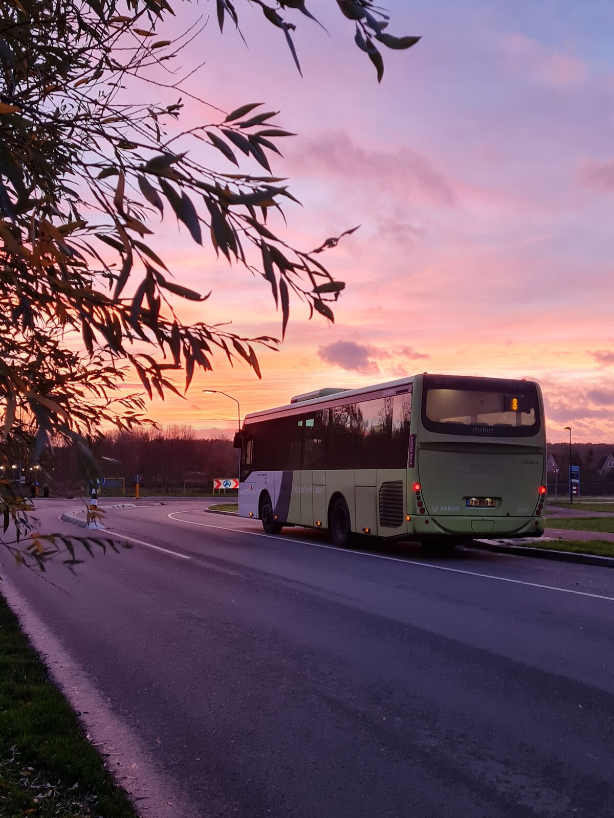 Arriva-bus rijdt op de weg onder een roze, oranje en paars gekleurde zonsondergang.