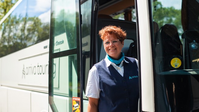 Buschauffeur Marijke staat lachend in de deuropening van haar bus waarop duidelijk 'Arriva Touring' staat. Buschauffeur Marijke staat lachend in de deuropening van haar bus waarop duidelijk 'Arriva Touring' staat.