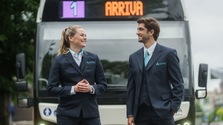 Een lachende man en vrouw in Arriva-uniforms staan voor een bus met het Arriva-logo en lijnnummer 1 zichtbaar op de achtergrond. Een lachende man en vrouw in Arriva-uniforms staan voor een bus met het Arriva-logo en lijnnummer 1 zichtbaar op de achtergrond.