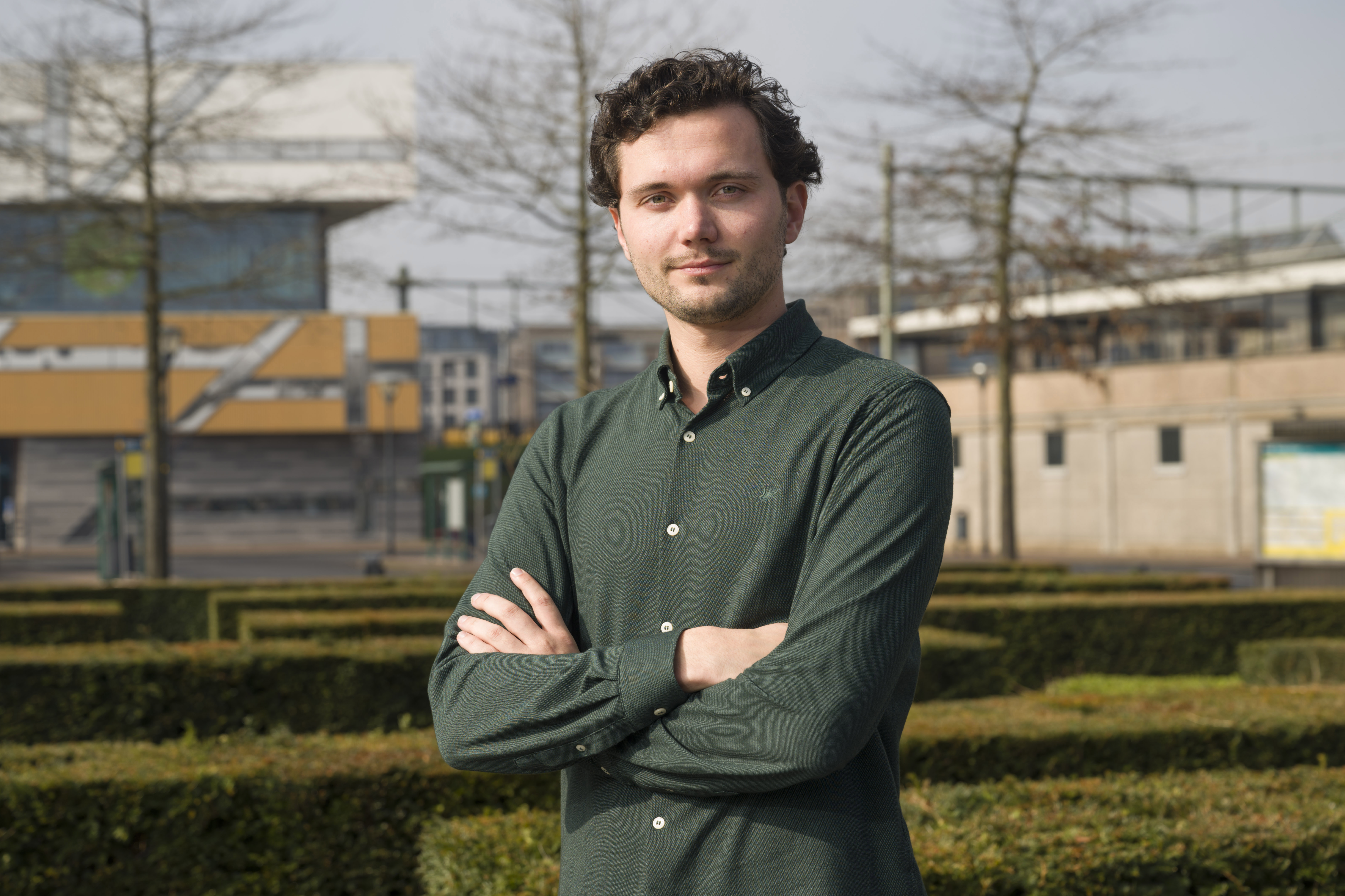 Man staat buiten voor een stedelijke achtergrond met zijn armen over elkaar 