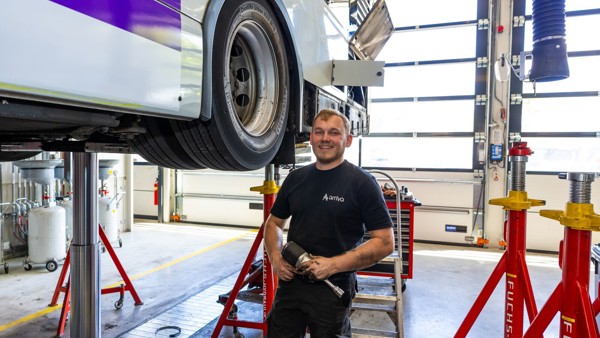 Monteur staat lachend bij wiel van een bus terwijl hij apparatuur vasthoudt. Monteur staat lachend bij wiel van een bus terwijl hij apparatuur vasthoudt.