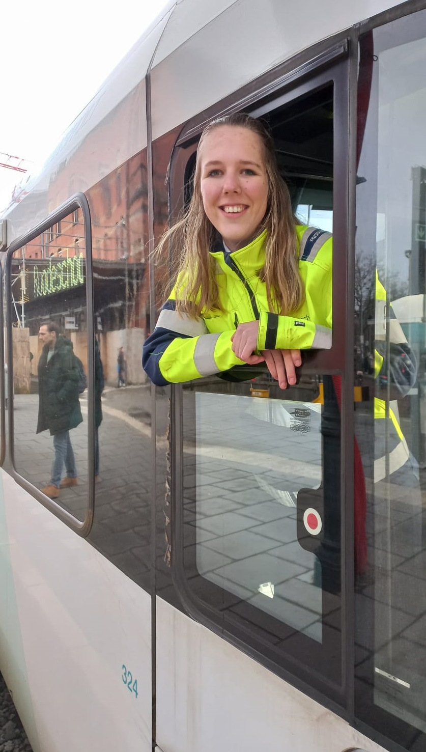 Treinmachinist in opleiding Nadine leunt uit het raampje van een Arriva-trein en lacht.