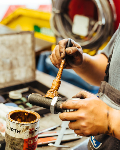 Monteur smeert een bout in met een kwast in een werkplaats met gereedschap op de achtergrond. Monteur smeert een bout in met een kwast in een werkplaats met gereedschap op de achtergrond.