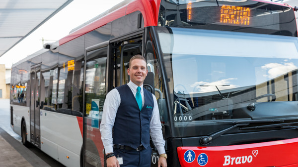Een lachende chauffeur in uniform staat voor een rode bus van Arriva. Een lachende chauffeur in uniform staat voor een rode bus van Arriva.