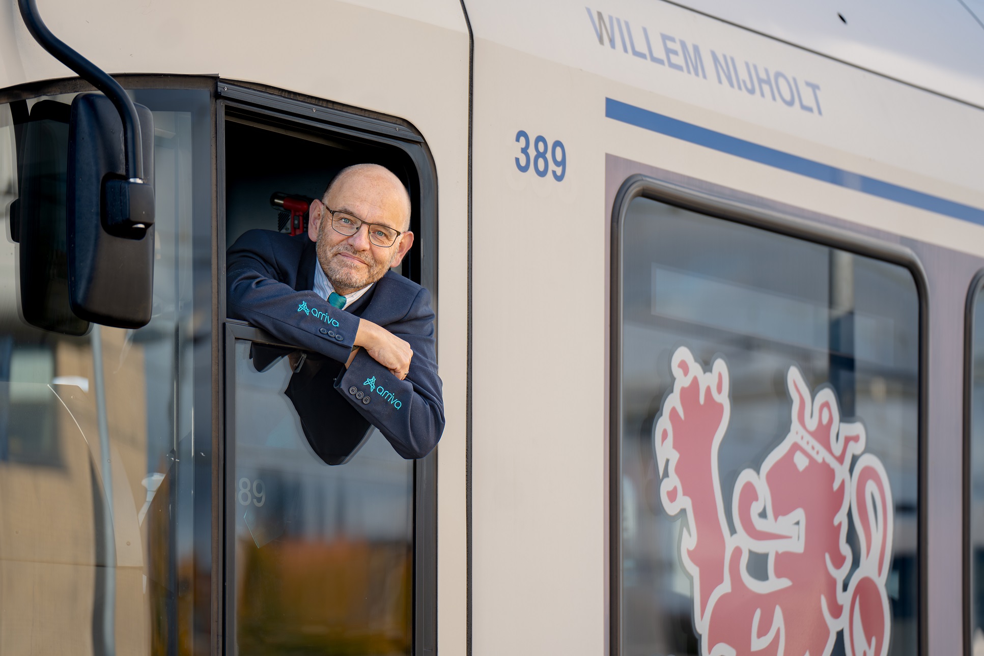 Machinist van middelbare leeftijd hangt uit het raam van een Arriva-trein 