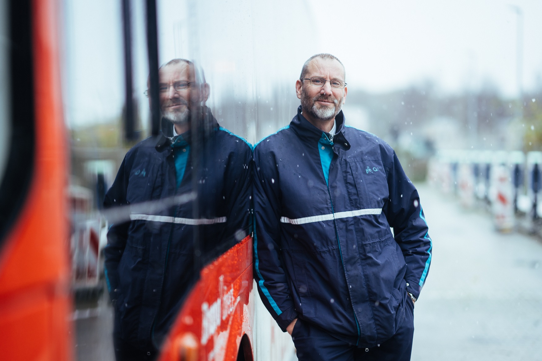 Buschauffeur Eric leunt in Arriva-uniform en tegen zijn bus aan terwijl het sneeuwt.