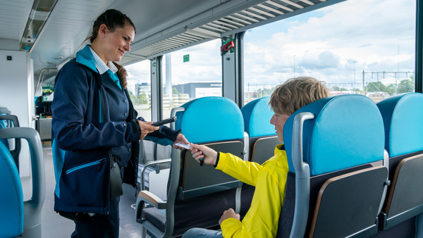 Vrouwelijke steward van Arriva geeft OV-chipkaart terug aan jonge reiziger in gele jas die in de trein zit. Vrouwelijke steward van Arriva geeft OV-chipkaart terug aan jonge reiziger in gele jas die in de trein zit.
