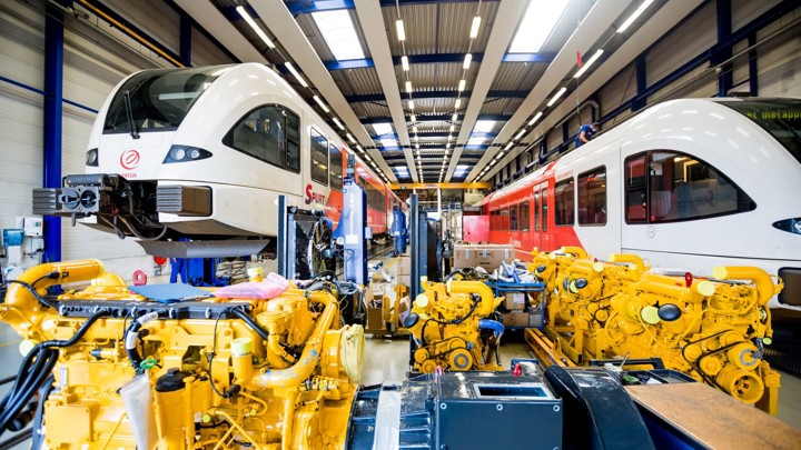 Twee Arriva treinen in een werkplaats met gele machines op de voorgrond. Twee Arriva treinen in een werkplaats met gele machines op de voorgrond.