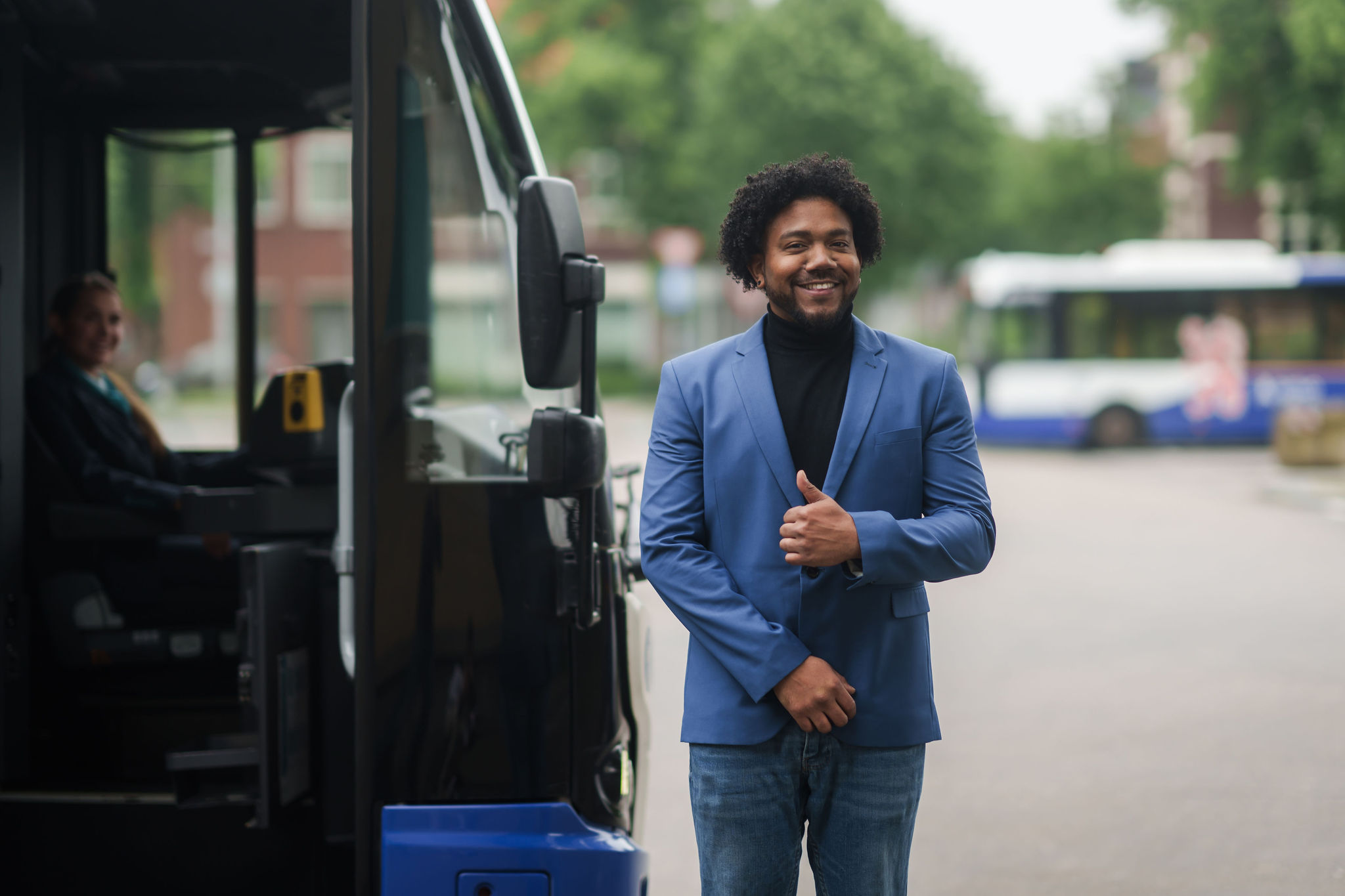 Een teammanager van Arriva in blauw pak staat lachend naast een bus.