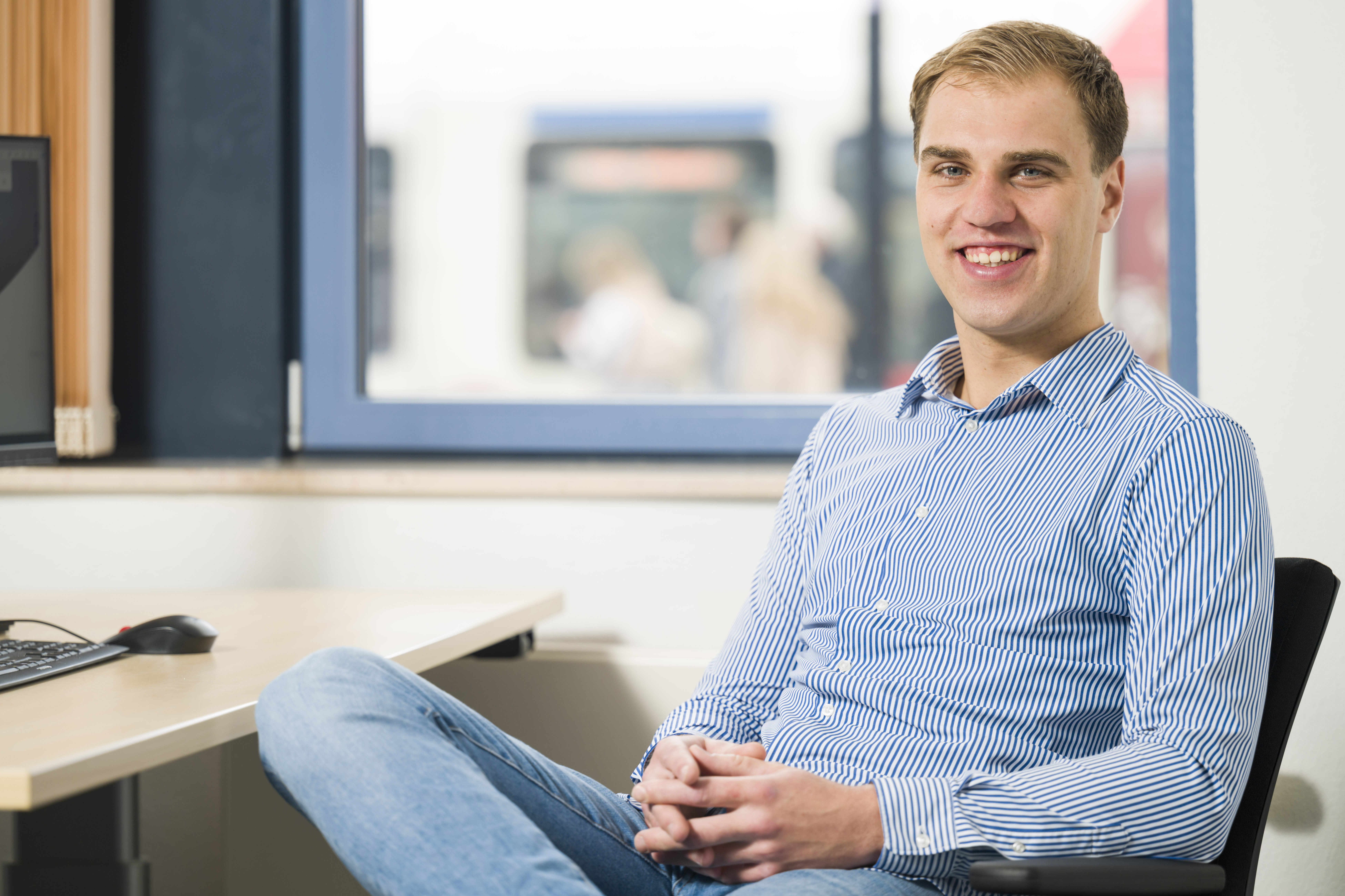 Glimlachende man zit in nonchalante houding achter een bureau 
