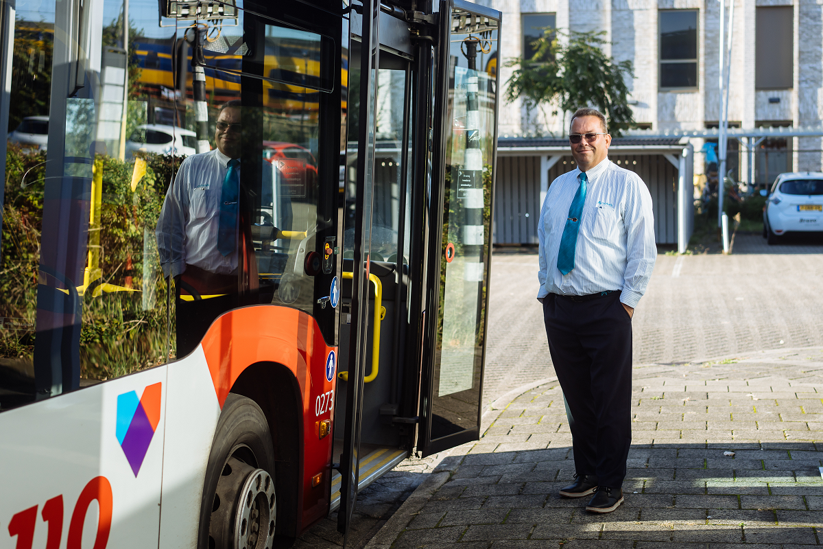 Buschauffeur van middelbare leeftijd staat naast een Arriva-bus