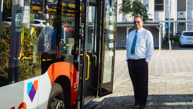 Buschauffeur van middelbare leeftijd staat naast een Arriva-bus Buschauffeur van middelbare leeftijd staat naast een Arriva-bus