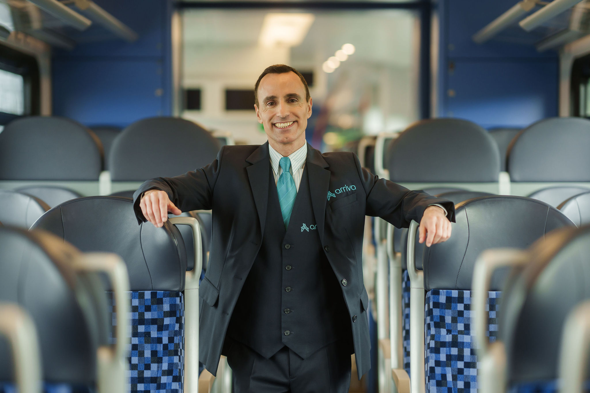 Machinist in uniform staat lachend tussen stoelen in trein.