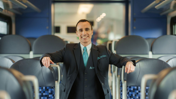 Machinist in uniform staat lachend tussen stoelen in trein. Machinist in uniform staat lachend tussen stoelen in trein.