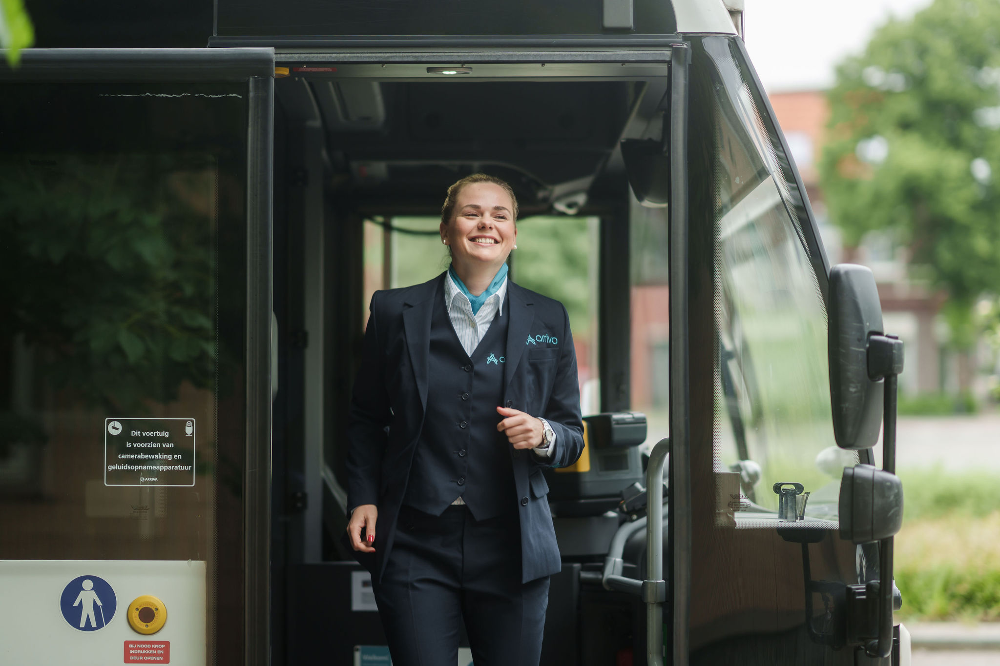 Een lachende buschauffeur in opleiding in Arriva-uniform stapt uit een bus, klaar om aan het werk te gaan.
