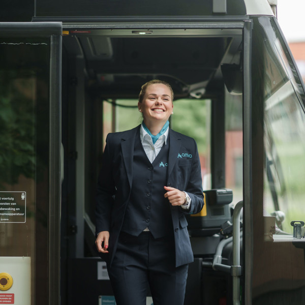 Een lachende buschauffeur in opleiding in Arriva-uniform stapt uit een bus, klaar om aan het werk te gaan. Een lachende buschauffeur in opleiding in Arriva-uniform stapt uit een bus, klaar om aan het werk te gaan.