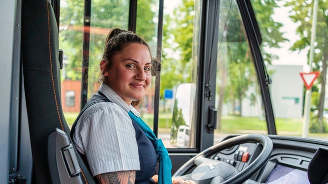 Buschauffeur Kelly van Arriva zit relaxed achter het stuur van haar bus en kijkt achterom naar haar reizigers. Buschauffeur Kelly van Arriva zit relaxed achter het stuur van haar bus en kijkt achterom naar haar reizigers.