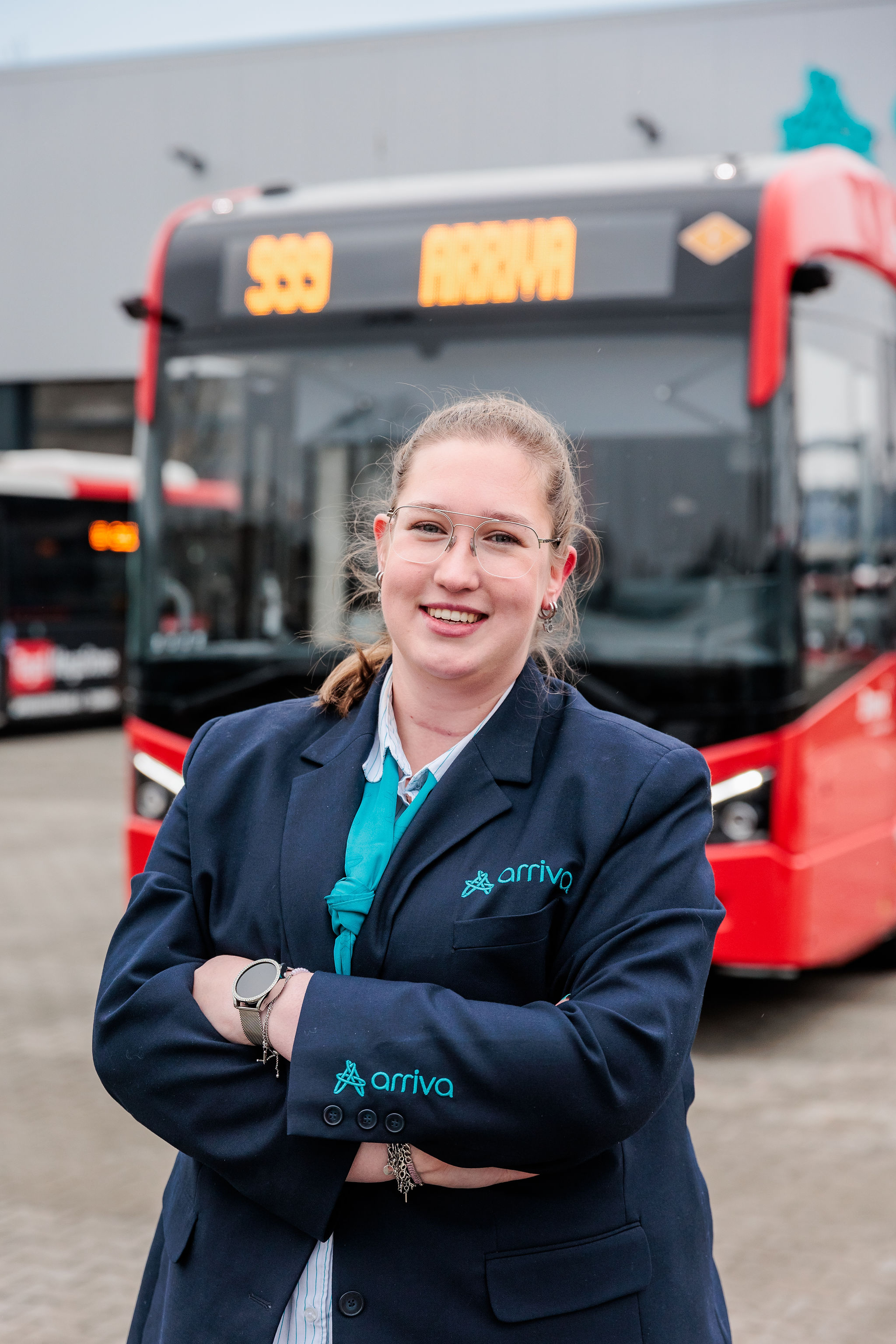 Lachende buschauffeur staat stoer met de armen overkruis voor de bus in Arriva uniform.