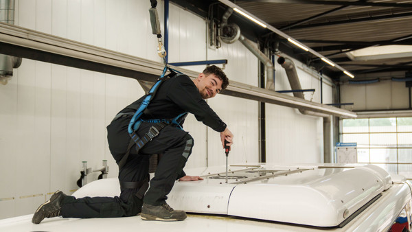 Een monteur van Arriva in veiligheidsharnas werkt op het dak van ene bus in een werkplaats en kijk lachend in de camera. Een monteur van Arriva in veiligheidsharnas werkt op het dak van ene bus in een werkplaats en kijk lachend in de camera.