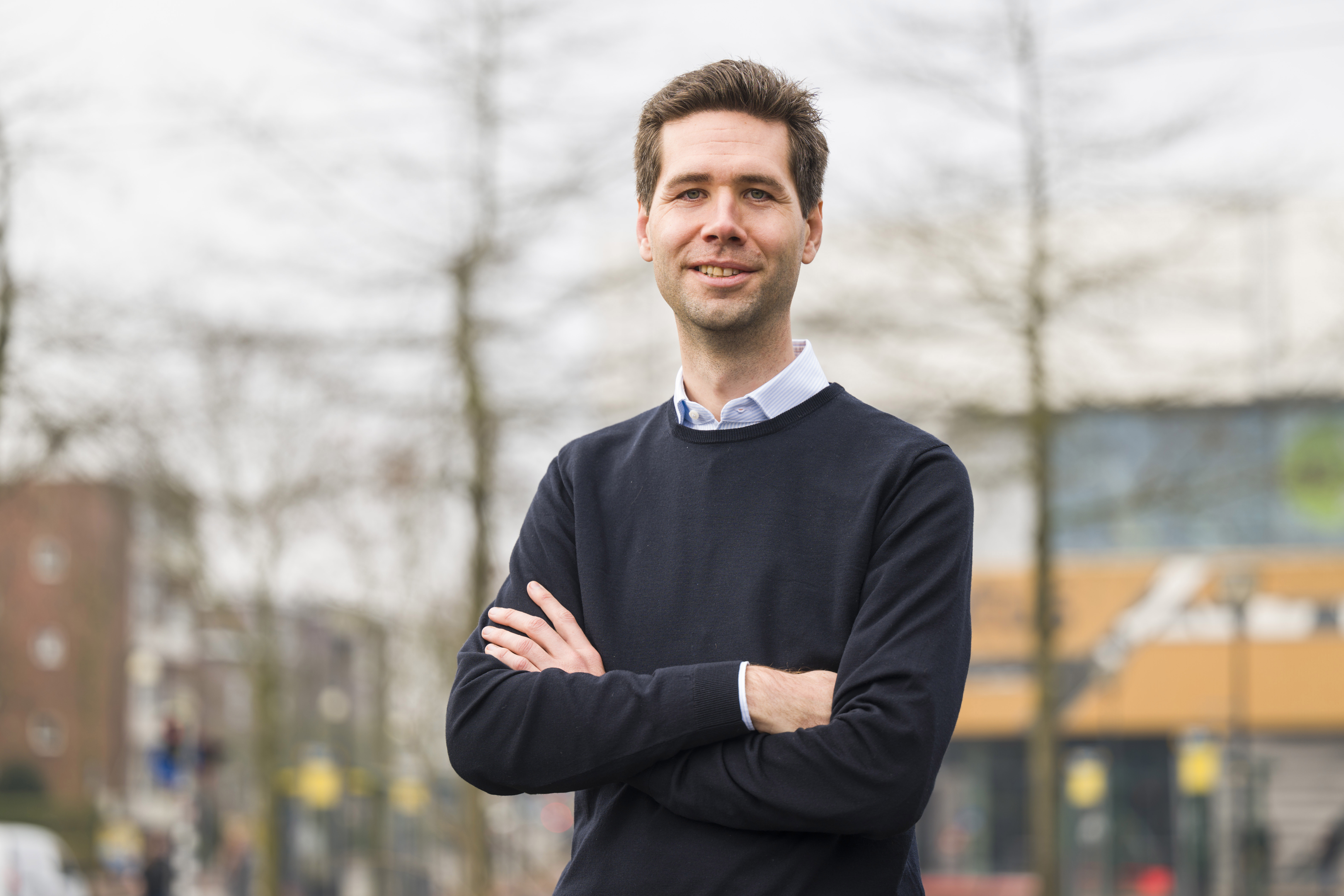 Glimlachende man staat buiten met zijn armen over elkaar