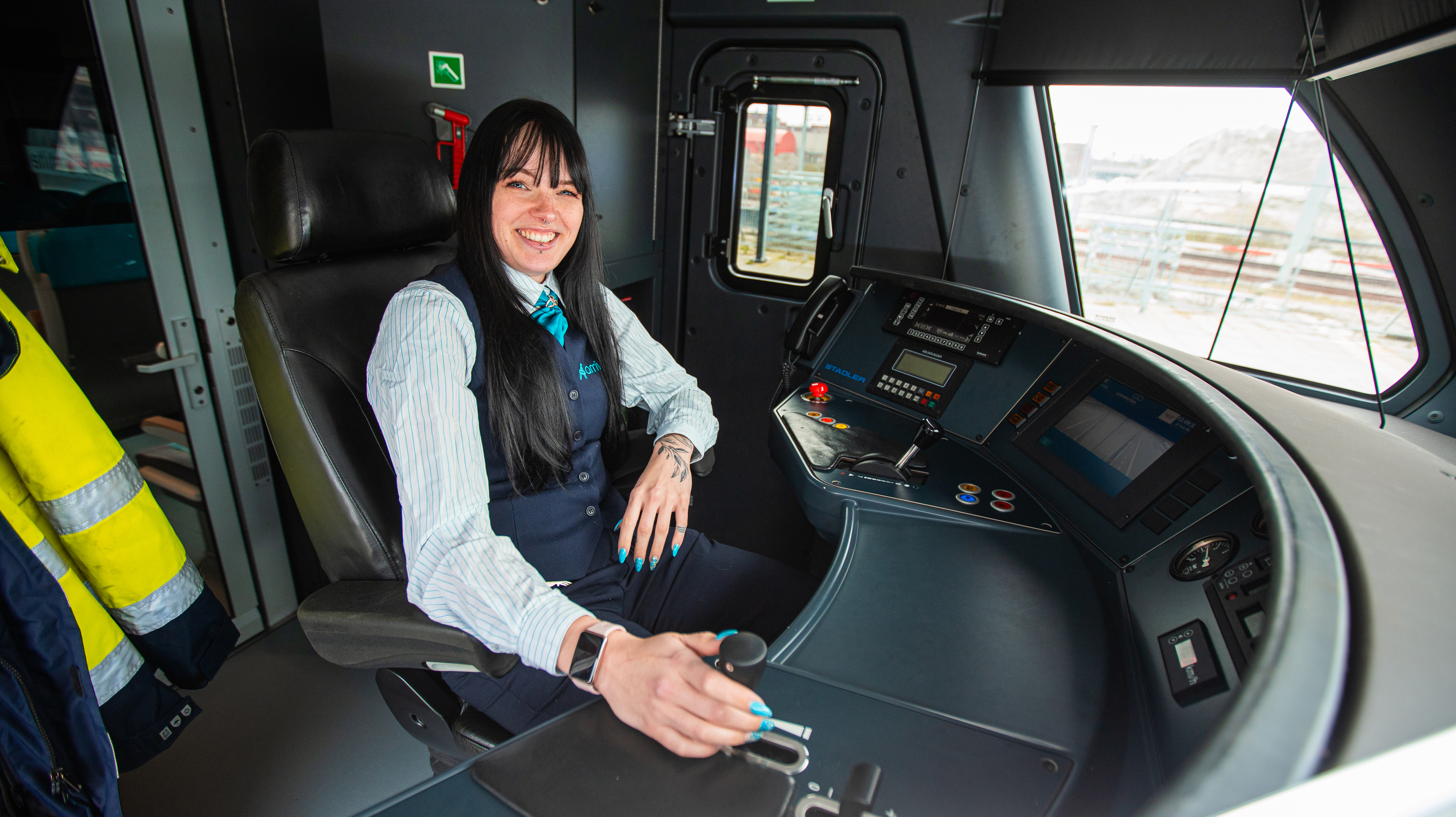 Machinist Shannon zit in haar Arriva-uniform achter het bedieningspaneel van een trein.