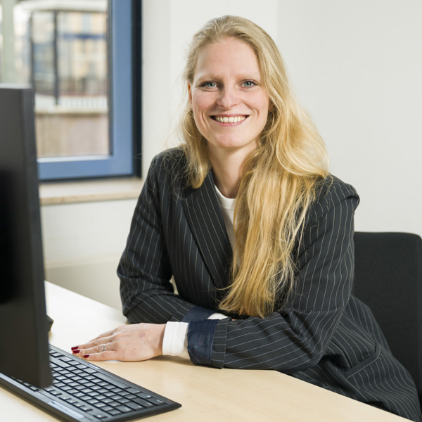 Vrouw zit lachend in zakelijke kleding achter een bureau met een computer Vrouw zit lachend in zakelijke kleding achter een bureau met een computer