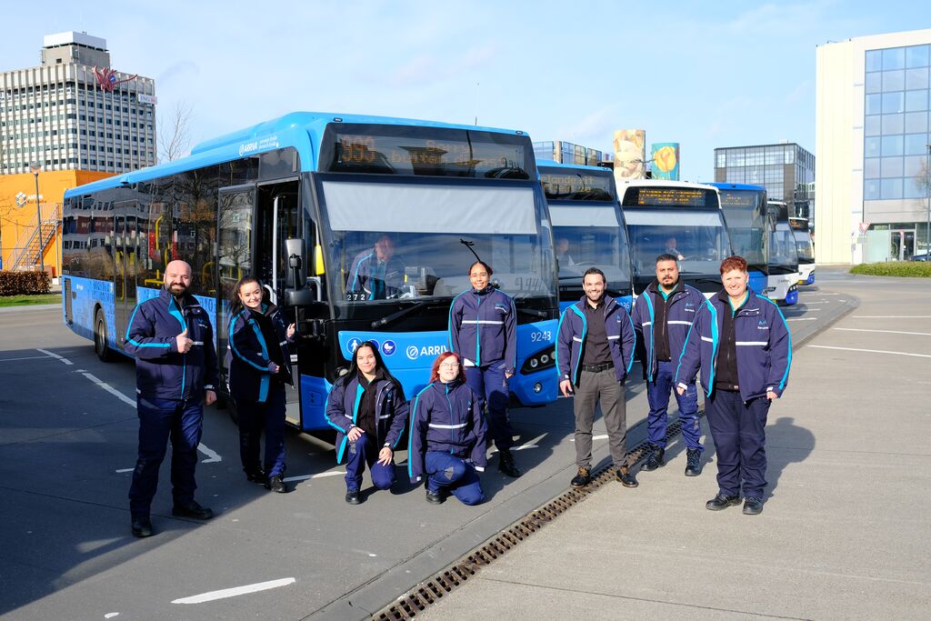 Achter servicemedewerkers poseren in uniform voor zes blauwe Arriva-bussen.